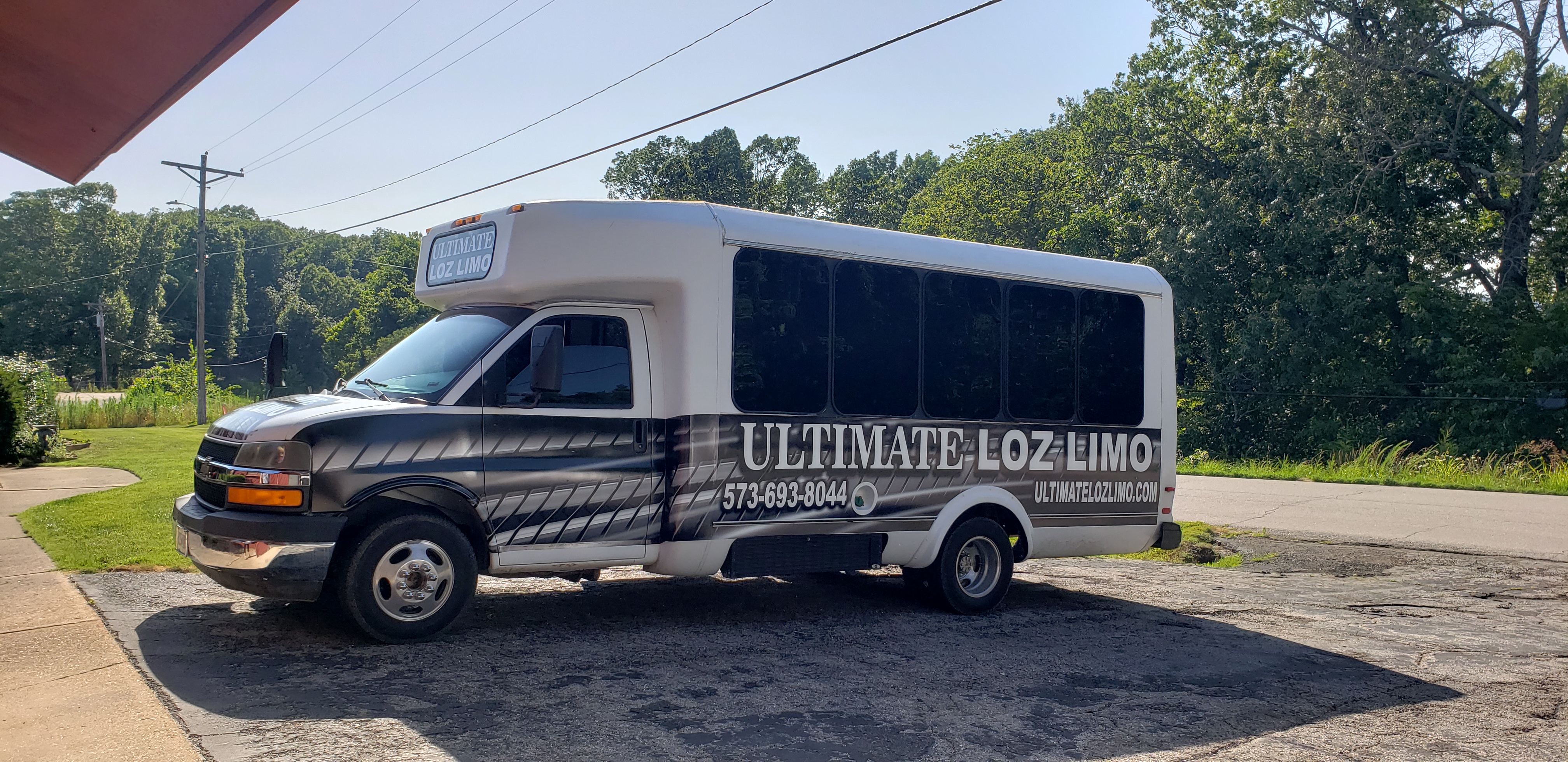 Silver and black party bus with tinted windows parked on a residential street surrounded by trees.